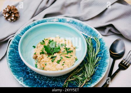 Risotto mit geriebenem Käse und Pilzstücken. Das Gericht ist mit frischen gehackten Petersilienblättern bestreut. Stockfoto