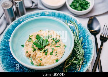 Risotto mit geriebenem Käse und Pilzstücken. Das Gericht ist mit frischen gehackten Petersilienblättern bestreut. Stockfoto