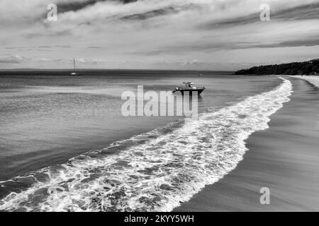 Hoher Kontrast in Schwarz-Weiß - kleines Motorboot auf weißem Sand am langen Strand in Jervis Bay Pazifikküste Australiens - Luftparadies Meereslandschaft. Stockfoto
