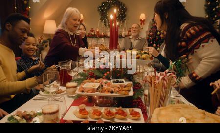 Glückliche große Familie, die zu Hause an einem Tisch sitzt und Weihnachten oder Neujahr feiert. Großmutter hat den Tisch mit traditionellem truthahn gedeckt. Warme Atmosphäre beim Weihnachtsessen mit der Familie. Heiligabend. Stockfoto