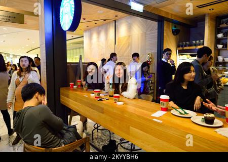 HONGKONG - 25. DEZEMBER 2015: Gäste des Starbucks Cafés. Die Starbucks Corporation ist ein amerikanisches globales Kaffeeunternehmen und eine Kaffeehauskette mit Sitz in Stockfoto