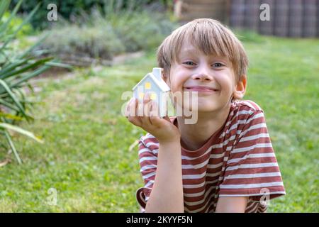 Kleines Haus in jungen Knabenhänden vor grünem Hintergrund von einem Baum in einem Garten. Stockfoto