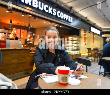 AMSTERDAM, NIEDERLANDE - 17. NOVEMBER 2015: Frau mit einer Tasse heißem Kaffee im Starbucks Café. Starbucks ist das größte Kaffeehausunternehmen der Welt, Stockfoto