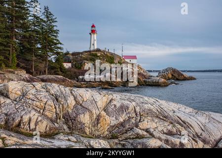 Wunderschöner Blick auf einen Leuchtturm an einer felsigen Küste während eines bewölkten Sonnenuntergangs. Historisches Wahrzeichen Atkinson Lighthouse in West Vancouver, Kanada. Stockfoto