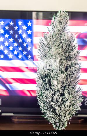 Weihnachtsbaum mit Computer im Hintergrund und US-Flagge auf dem Bildschirm. Stockfoto