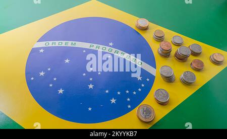 Übersetzung 'Bestellfortschritt' brasilianische Flagge mit brasilianischen echten Münzen, Konzept des Verfalls brasilianischen Geldes. Stockfoto