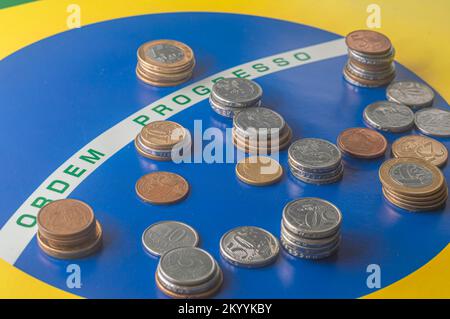 Übersetzung 'Bestellfortschritt' brasilianische Flagge mit brasilianischen echten Münzen, Konzept des Verfalls brasilianischen Geldes. Stockfoto