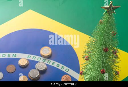 Übersetzung 'Bestellfortschritt' brasilianische Flagge mit brasilianischen echten Münzen und einem weihnachtsbaum fiel neben das Year-End-Konzept. Stockfoto