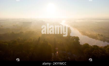 Waldparks, Flüsse und viele Hochhäuser in der Stadt am frühen Morgen bei Sonnenaufgang im Sommer. Hell leuchtende Sonne, klarer wolkenloser Himmel und Morgennebel Sonnenstrahlen und Schatten Luftdrohnenlandschaft Stockfoto