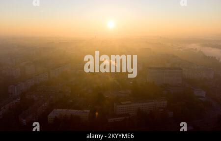 Waldparks, Flüsse und viele Hochhäuser in der Stadt am frühen Morgen bei Sonnenaufgang im Sommer. Hell leuchtende Sonne, klarer wolkenloser Himmel und Morgennebel Sonnenstrahlen und Schatten Luftdrohnenlandschaft Stockfoto