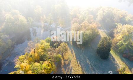 Luftfliegen über Bäume mit gelben Blättern, See, Säulen und Wanderungen an sonnigen Herbstvormittagen im Park. Helles Sonnenlicht, glänzende Sonnenstrahlen und übermäßige Sonneneinstrahlung. Wunderschöner natürlicher Hintergrund Stockfoto