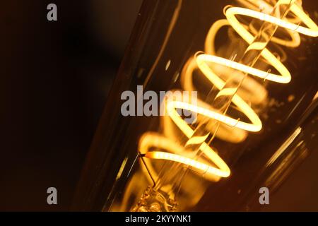 Makro des gelben Spiralglühlampen-Glühfadens bei Nacht. Stockfoto