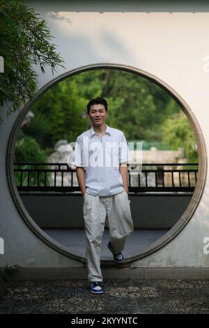 Ein hübscher junger chinesischer Mann steht am Mondtor im traditionellen chinesischen Garten Stockfoto