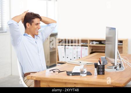 Ich sehe mir die Online-Präsenz seiner Firma an. Ein entspannter Geschäftsmann, der mit den Armen hinter dem Kopf in seinem Büro sitzt. Stockfoto