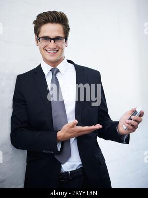Darf ich Ihnen die Zukunft der Geschäftstechnik vorstellen? Ein gutaussehender junger Geschäftsmann, der ein Handy präsentiert. Stockfoto