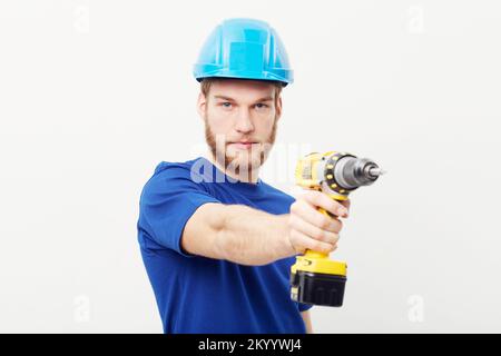Optimale Nutzung von Elektrowerkzeugen. Porträt eines ernsthaft aussehenden jungen Mannes, der einen Schutzhelm trägt und eine Bohrmaschine in der Hand hält. Stockfoto