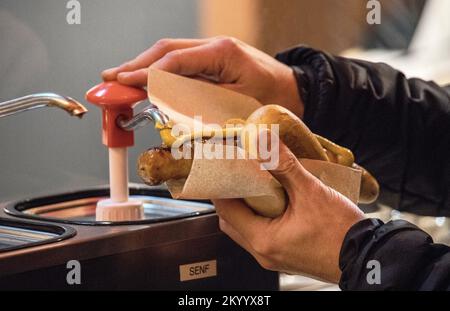 Köln, Deutschland. 02.. Dezember 2022. Auf dem Weihnachtsmarkt am Kölner Dom pumpt ein Besucher Senf in einem Brötchen auf eine Bratwurst. An vielen Orten in Nordrhein-Westfalen sind die Weihnachtsmärkte genauso belebt wie vor der Corona-Pandemie. Zahlreiche Touristen reisen dieses Jahr wieder für dieses besondere Erlebnis. (Zu dpa: „Sehnsucht und Gemütlichkeit: Weihnachtsmärkte wie vor Corona“) Kredit: Sascha Thelen/dpa/Alamy Live News Stockfoto