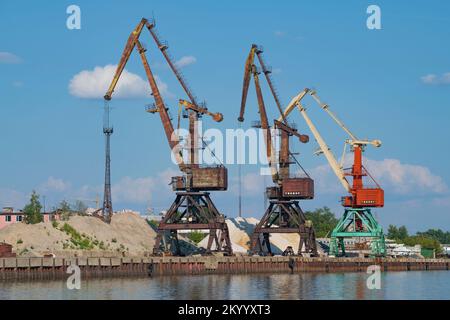 TSCHEREPOVETS, RUSSLAND - 04. AUGUST 2022: Drei Hafenkräne im Flusshafen an einem sonnigen Sommertag Stockfoto