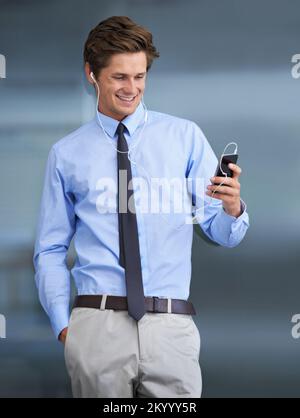 Er wählt einige seiner Favoriten aus. Ein attraktiver junger Geschäftsmann, der sein Smartphone als mp3-Player benutzt. Stockfoto
