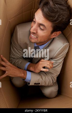 Gefangen in seiner Karriere. Konzeptaufnahme eines jungen Geschäftsmannes, der in einem Karton gefangen ist. Stockfoto