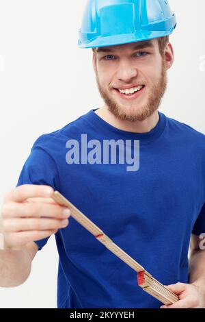 Durchführen von Messungen. Porträt eines glücklichen jungen Mannes mit Schutzhelm und Tischlerlineal. Stockfoto