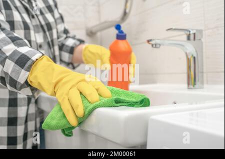 Waschbecken und Wasserhahn im Bad werden mit Waschmittel gereinigt. Person, die Hausarbeiten erledigt und zu Hause die Toilette reinigt. Reinigungsservice. Zimmermädchen putzen Stockfoto