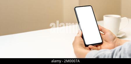 Mockup Handy. Hände der Frau mit Handy vor dem Hintergrund der gelben Wand und Tasse Kaffee. Mockup-Bild der Hände, die das Mobiltelefon mit halten Stockfoto