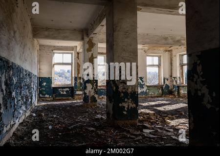 Verlassene und zerstörte Büros und Hallen, ein zerstörtes Industriegebäude, ein Haus mit zerbrochenen Fenstern, Lichtstrahlen in einem zerstörten Raum. Stockfoto