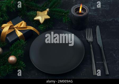 Weihnachten, Silvester Tischdecken in Schwarz. Schwarze Platte, Gabel, Messer, Tannenbaum, Kerze, Geschenkbox und Spielzeug. Draufsicht, Modell. Stockfoto