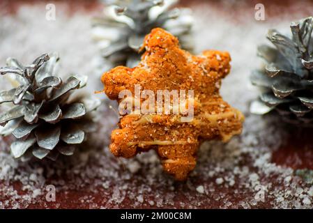 Drei silberne Kiefernzapfen und Butterkeks in Form eines Sterns auf Schnee, weihnachtsdekoration. Stockfoto