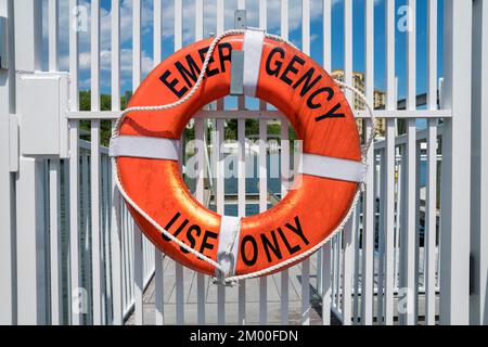 Destin, Florida - Rettungsring mit Notsymbol. Das Rettungsboot hängt an einem weißen Gitter vor dem Blick auf das Wasser im Hintergrund Stockfoto