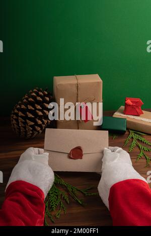 Der Weihnachtsmann liest am Heiligabend vor einer grünen und holzgrünen Kulisse Kinderwünsche Stockfoto