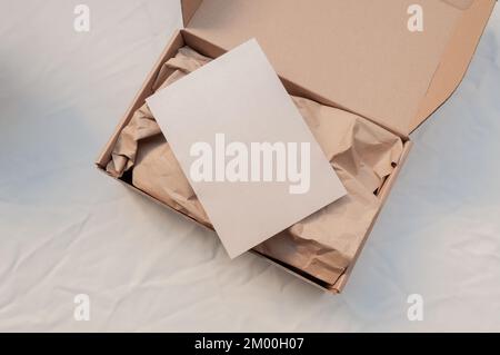 Kraftkasten für kleine Unternehmen aus der Vogelperspektive mit weißer Postkarte (10 x 15 cm) und Kraftpapier. Auspacken für E-Commerce Stockfoto