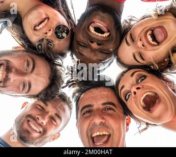 Junge Leute, die in die Kamera schauen und lachen, multirassische Gruppe von Freunden, die im Kreis stehen und vor der Kamera lächeln, Selfie-Kreis mit unterschiedlicher ethnischer Herkunft Stockfoto