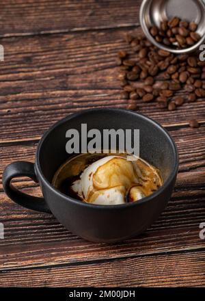 Espresso mit Eiscreme in schwarzem Porzellanbecher auf Holztisch. Affogato-Kaffee Stockfoto