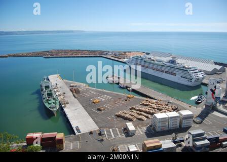 Napier Port in Hawke's Bay, Neuseeland, Februar 2010. Protokolle warten auf Export. Ein Frachtschiff ist vor Anker. Kreuzfahrtschiff Pacific World (als Sun Princess) ist angedockt. Stockfoto