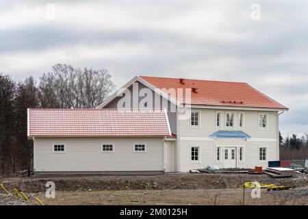 Bild eines unvollendeten Holzhauses im skandinavischen Stil mit weißen Seitenwänden und traditionellem orangefarbenem Dach Stockfoto