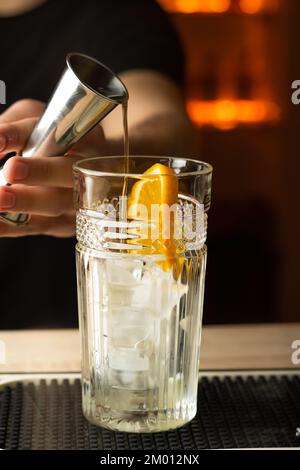 Der Barkeeper gießt einen Gin aus dem Stahlrüttler auf das Glas auf der Theke. Speicherplatz kopieren Stockfoto