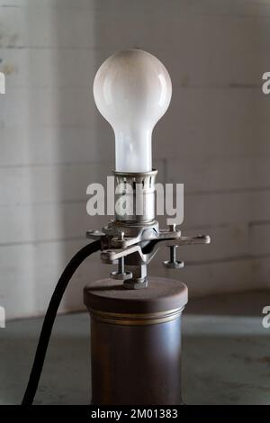 Abbildung: Alte weiße Glühlampe auf dem alten Metallhalter mit Stromkabel Stockfoto