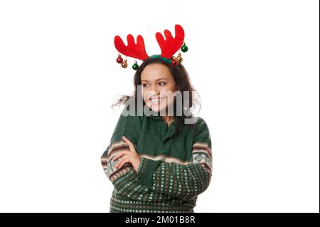 Fröhliche Frau, trägt Hirschgeweih und grünen Pullover mit Weihnachtsmuster, lacht, schaut zur Seite in die Kopierfläche Stockfoto