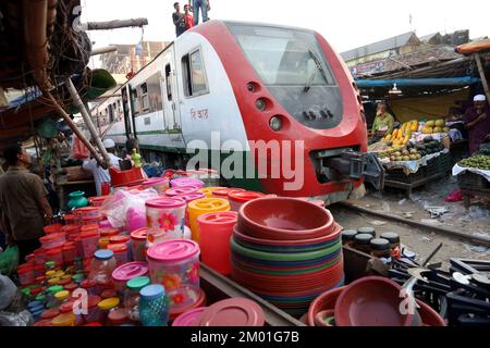Dhaka, Dhaka, Bangladesch. 3.. Dezember 2022. Ein Pendlerzug fährt durch den Jurain Railgate Market in Dhaka. Die Händler verkaufen Obst und Gemüse nur wenige Zentimeter von der Zuglinie entfernt. (Bild: © Syed Mahabubul Kader/ZUMA Press Wire) Stockfoto