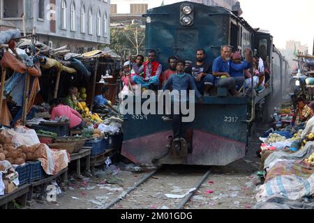 Dhaka, Dhaka, Bangladesch. 3.. Dezember 2022. Ein Pendlerzug fährt durch den Jurain Railgate Market in Dhaka. Die Händler verkaufen Obst und Gemüse nur wenige Zentimeter von der Zuglinie entfernt. (Bild: © Syed Mahabubul Kader/ZUMA Press Wire) Stockfoto