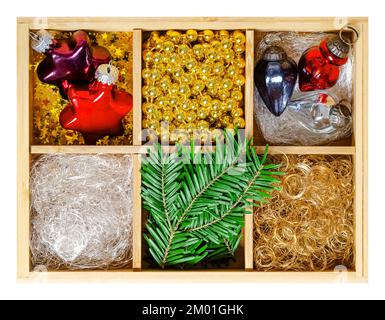 Weihnachtsschmuck in Holzkiste. Stern- und Eichelförmige Weihnachtsglaszwiebeln, silberne und goldene Engelhaare, goldene Perlengürtel und Tannenzweige. Stockfoto