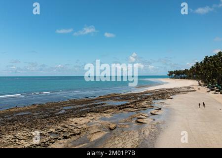 Touristen laufen bei Ebbe am Strand entlang mit Riffen zwischen Strand und Meer. Stockfoto