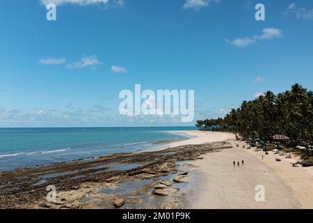 Touristen laufen bei Ebbe am Strand entlang mit Riffen zwischen Strand und Meer. Stockfoto