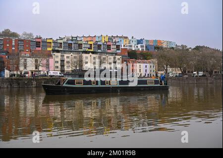 Ein neues Liveboard-Widebeam-Boot, das durch die Bristol Docks fährt, vorbei an einer Reihe farbenfroher Häuser im Hintergrund. Stockfoto