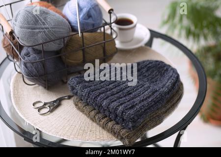 Gestrickte Hüte und Strähne aus Wolle in einem Korb auf einem Tisch Stockfoto