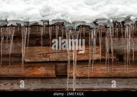 Eiszapfen hängen vom schneebedeckten Dach eines alten Holzhauses Stockfoto