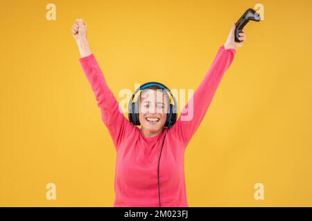 Eine schöne Frau, die Spiele spielt und Kopfhörer trägt, mit isoliertem gelbem Hintergrund. Stockfoto