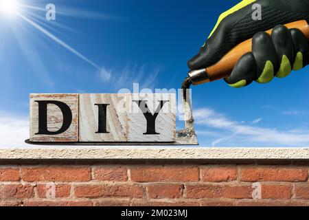 Arbeiter mit Schutzhandschuhen, der eine schmutzige Kelle und den selbstgemachten Text aus Holzblöcken über einer Ziegel- und Marmorwand hält. Stockfoto